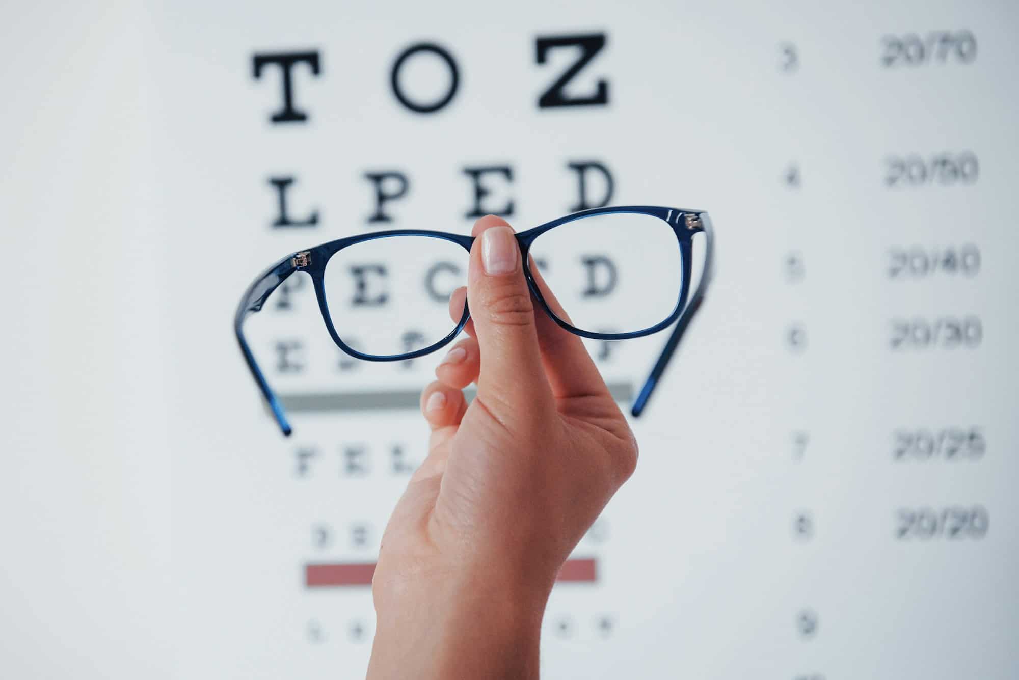 Woman hand holding the glasses on background of the eye chart